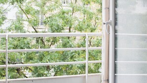 A view through a window with metal bars, a white door, and greenery outside. - Charming, bright studio in the heart of Paris (Paris)