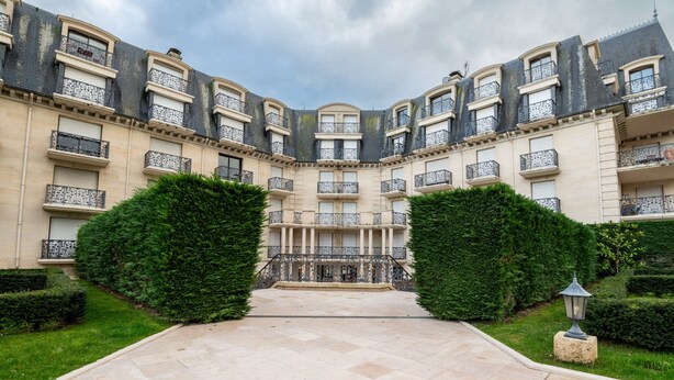 Un bâtiment symétrique doté d’une cour intérieure, avec un chemin pavé et des haies soigneusement taillées.