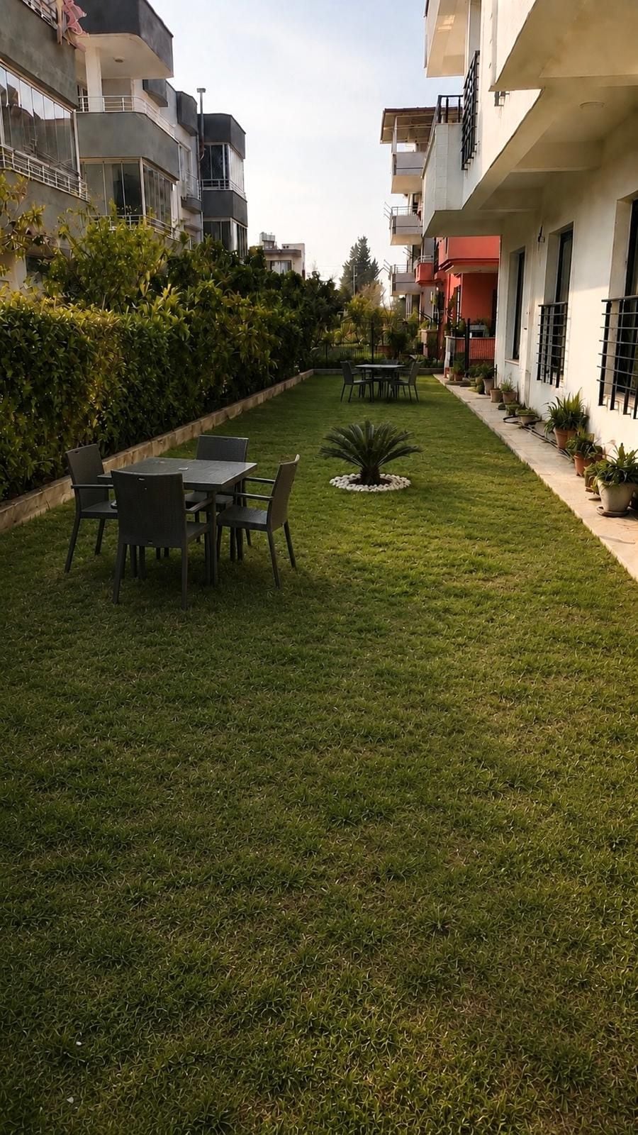 Un patio con una mesa y sillas, rodeado de un césped cuidado y plantas en macetas.