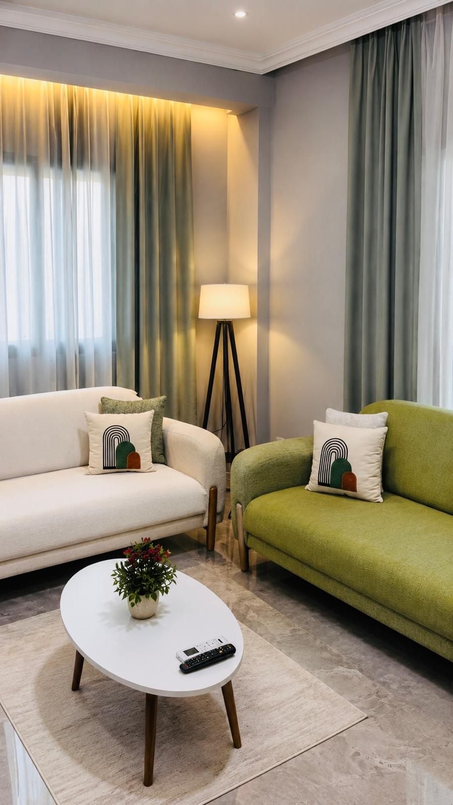 A modern living room with a sofa, a green sofa, a lamp, and a remote control on a coffee table.