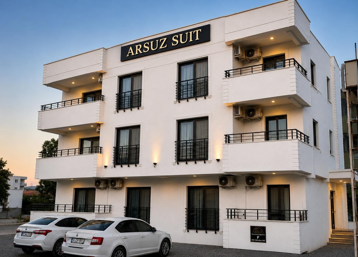 Kyseessä on useita kerroksia sisältävä rakennus, jossa on kyltti, jossa lukee »ARSUZ SUIT», mikä viittaa hotelliin tai vastaavaan majoitusliikkeeseen. Rakennuksessa on useita parvekkeita, joissa on kaiteet, ja sen arkkitehtuuri on modernia.