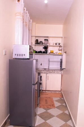 Eine kleine Küche mit Kühlschrank, Mikrowelle und verschiedenen Küchenutensilien in Regalen.