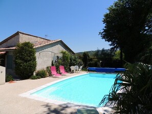 Ein Schwimmbad mit Fliesen umgeben, mit einem Haus mit geneigtem Dach und einer Satellitenschüssel.
