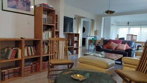 Ein geräumiges Wohnzimmer mit einer großen Bücherwand, einer gemütlichen Sofagarnitur und einem Fernseher.