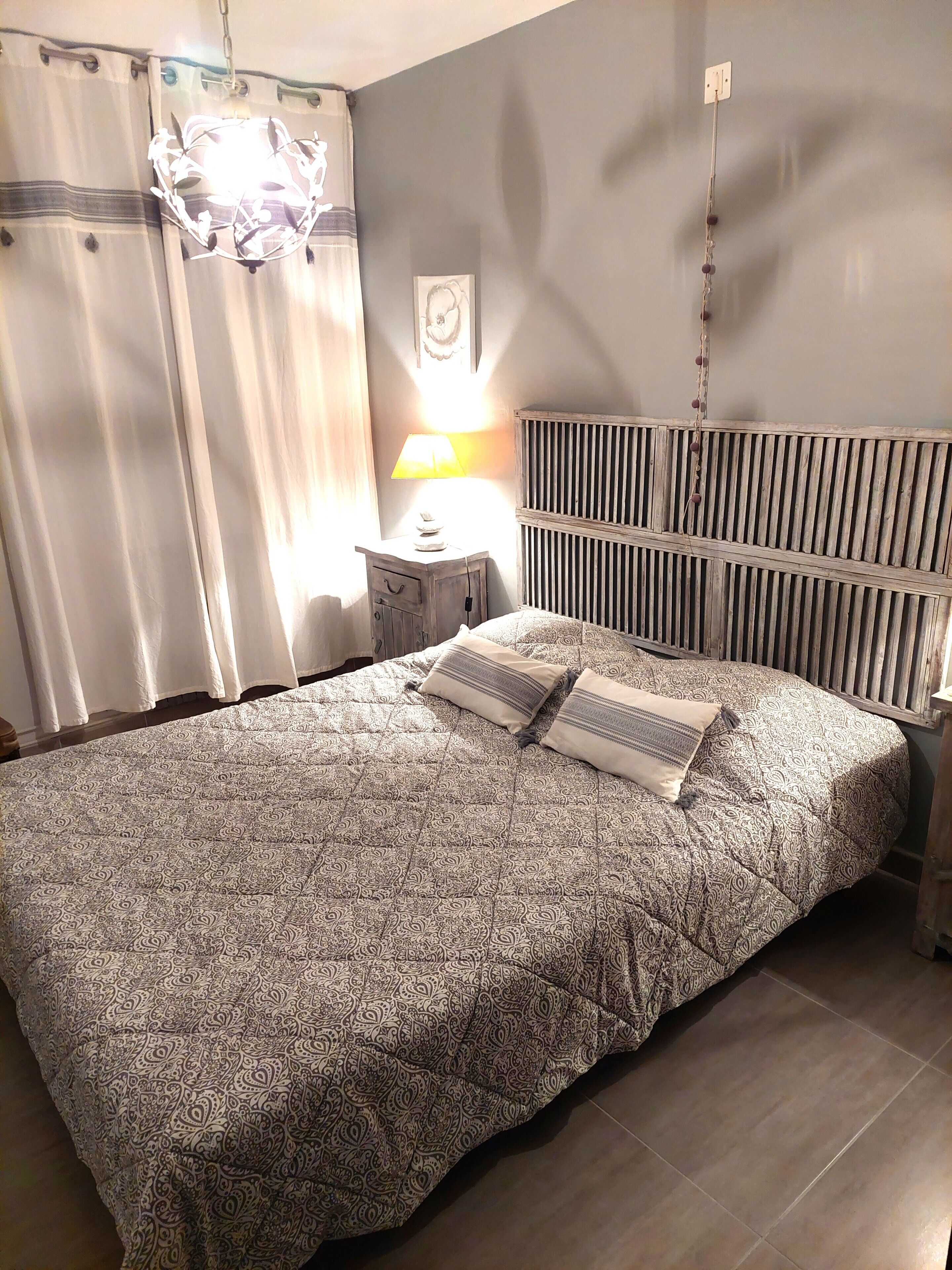 A bedroom with a bed, a bedside table with a lamp, a radiator, and curtains.
