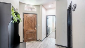 A hallway with a wooden door, a black cabinet with plants, and a light-colored floor.
