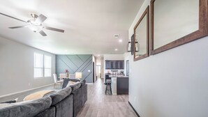 A modern kitchen with a central island, a dining area with a sofa, and a hallway leading to a staircase.