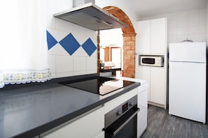 A kitchen with a black countertop, white cabinets, a microwave, and a refrigerator. - Cortijo Encarni (Nerja)