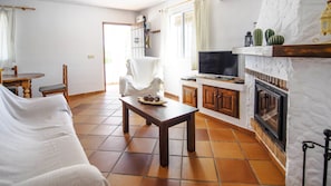 A living room with a sofa, a wooden coffee table with decorative items, a television, and a fireplace. - Cortijo Encarni (Nerja)