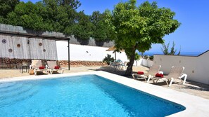 A pool area with lounge chairs and a table, surrounded by a white wall and a stone wall. - Cortijo Encarni (Nerja)
