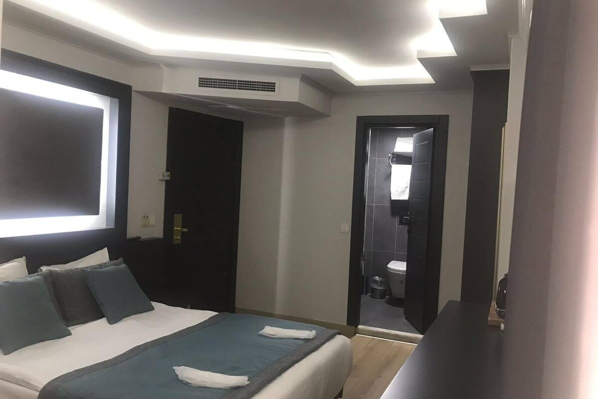 A hotel room with a bed, bedside table, and a bathroom visible through an open door.