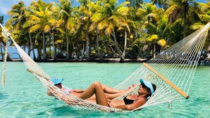 Uma rede sobre uma piscina azul-turquesa límpida, cercada por palmeiras.