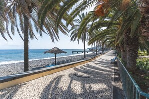 A paved walkway with palm trees, a beach, and a thatched-roof structure. - Casa Vista Azul by Atlantic Holiday (Santa Cruz)