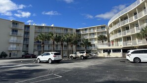 Un hotel de varios pisos con estacionamiento, varios coches y palmeras.