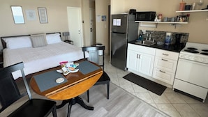 Habitación de hotel con cama, mesa de comedor con sillas, y área de cocina con refrigerador, microondas, estufa y alacenas.