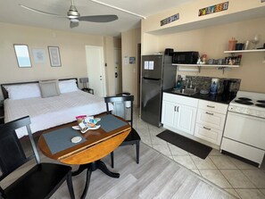 A hotel room with a bed, a dining table with chairs, a kitchen area with a refrigerator, microwave, stove, and cabinets. - Oceanfront Oasis studio Condo at the Beach (Daytona Beach)
