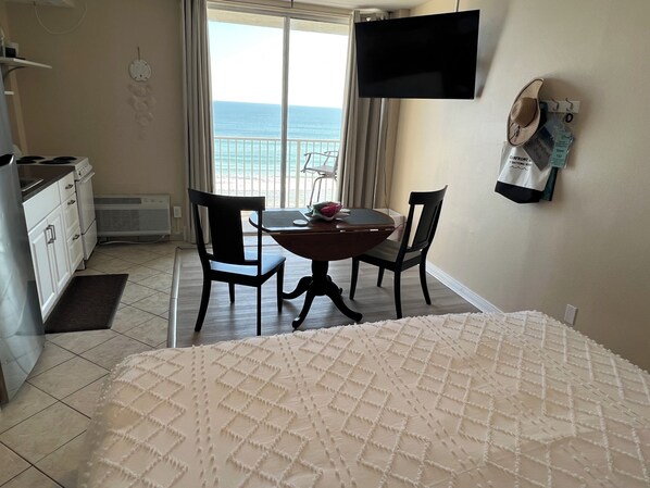 Une chambre d’hôtel avec un lit, une table à manger avec des chaises, un téléviseur fixé au mur et une vue sur l’océan par la fenêtre.