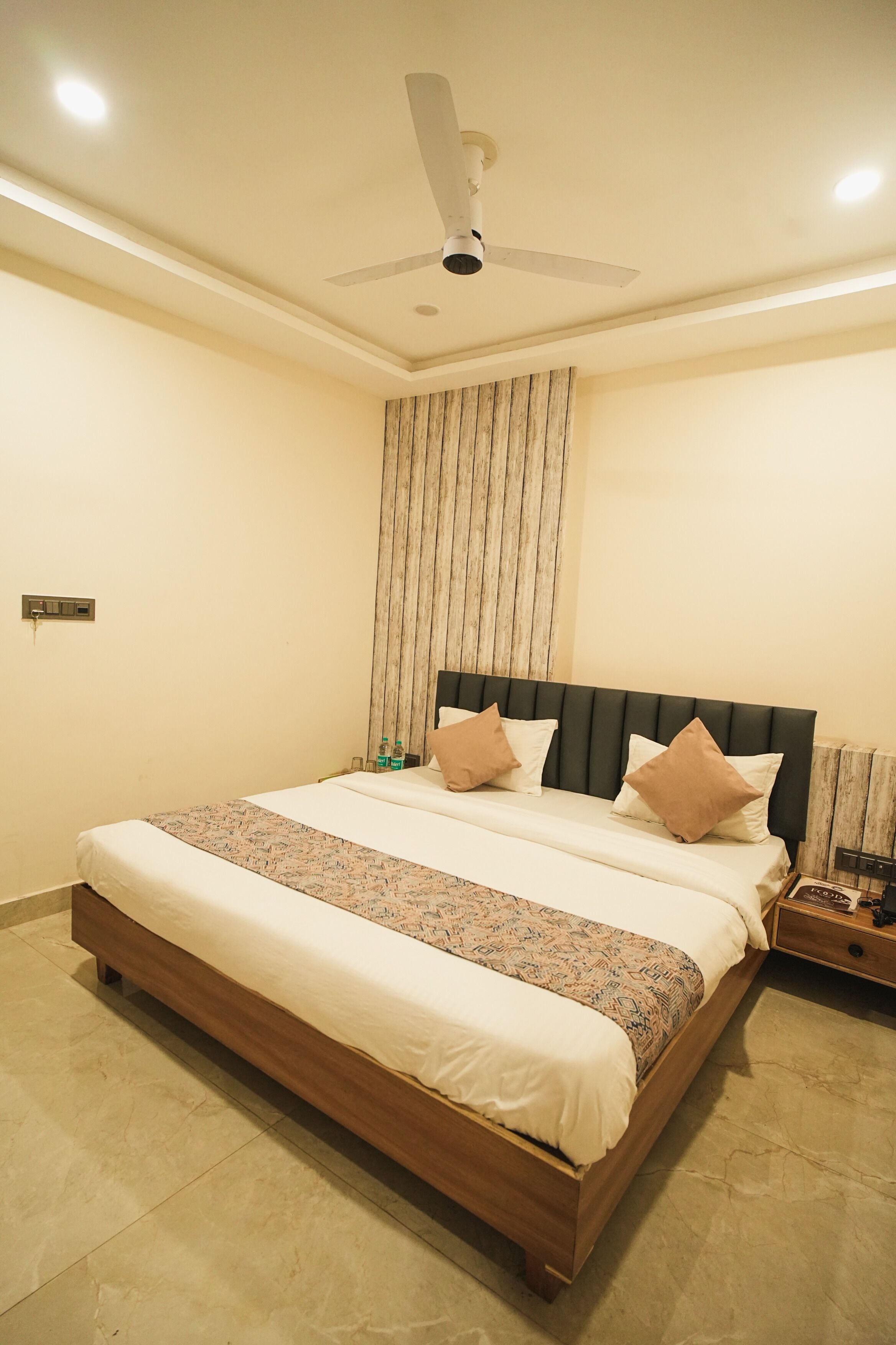 A bedroom with a large bed, a ceiling fan, and a nightstand with a lamp.