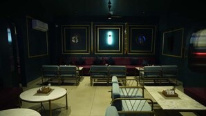 Une pièce faiblement éclairée, avec une rangée de tables et de chaises, un canapé et un mur orné de tableaux.
