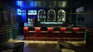Un espace bar avec un comptoir rouge, de nombreux tabourets et un écran de télévision.