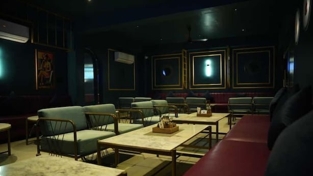 Un restaurant à la lumière tamisée, avec des banquettes et des tables, des climatiseurs et des œuvres d’art encadrées accrochées aux murs.