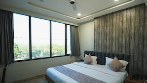 Une chambre d’hôtel moderne avec un grand lit, un ventilateur de plafond et une vue sur la verdure par la fenêtre.