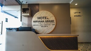 Un comptoir d’accueil d’hôtel avec un panneau circulaire indiquant le nom « HÔTEL NIRVANA GRAND » et les heures d’arrivée et de départ.