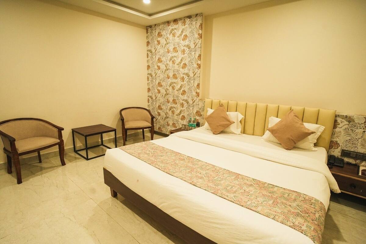 Ein Hotelzimmer mit einem großen Bett, zwei Stühlen, einem kleinen Tisch und einem gemusterten Vorhang.