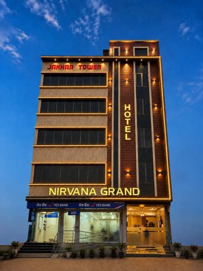 Ein Hotel mit moderner Fassade, einem gut sichtbaren Schild für 'NIRVANA GRAND' und einem Eingangsbereich, unter dem sich eine Bankfiliale befindet.