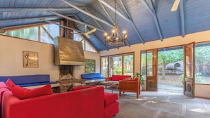 A spacious living area with a red sofa, a blue sofa, and a wooden table. There is a large window with a view of the outdoors. - Lodge Los Naranjos de Mallarauco  (Melipilla)