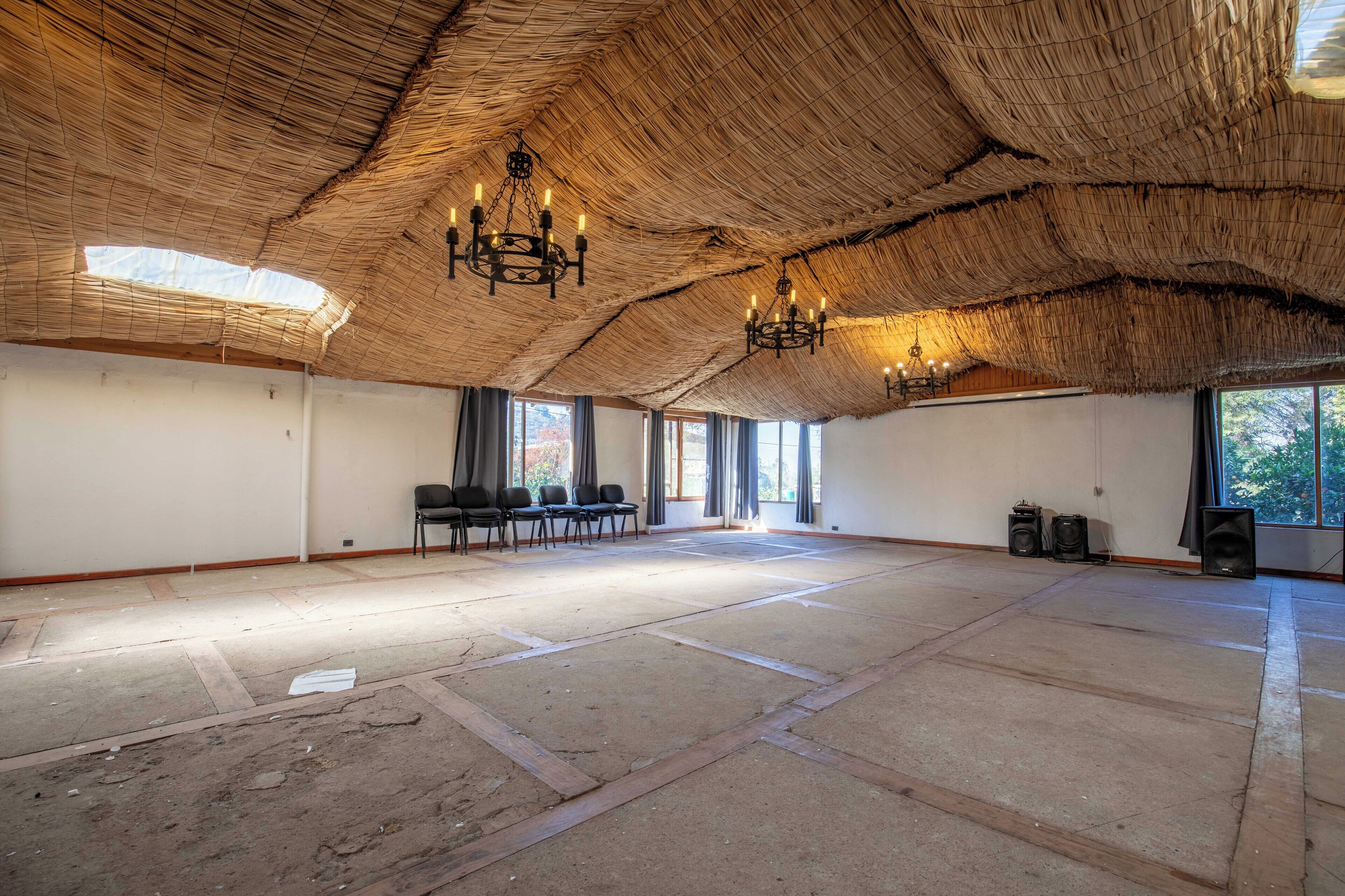 A spacious room with a thatched ceiling, multiple chandeliers, and a large window providing natural light.