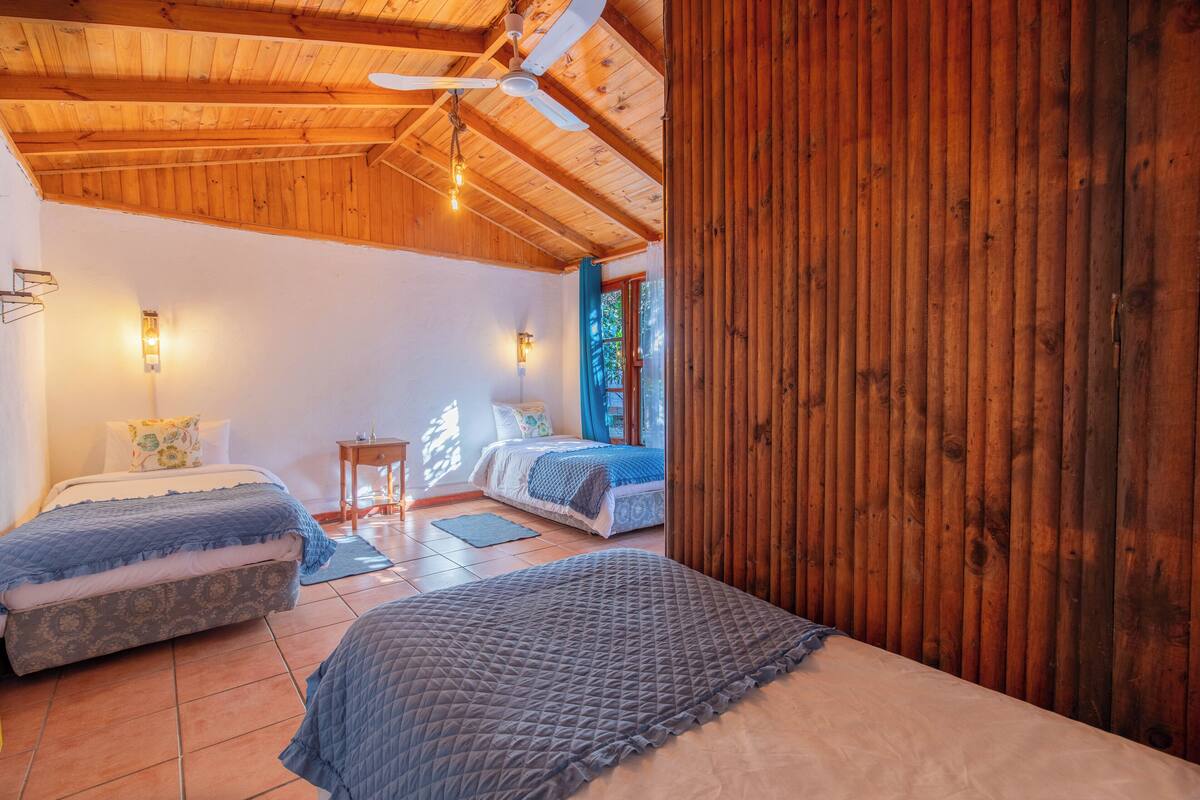 A cozy bedroom with two beds, wooden ceiling beams, and a large window.