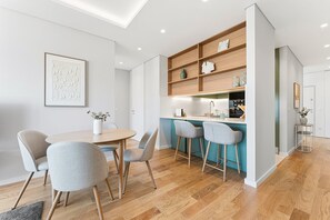 A modern kitchen with wooden shelves, a central island with bar stools, and a dining area with a round table and chairs. - GuestReady - Porto Retreat with Terrace (Porto)