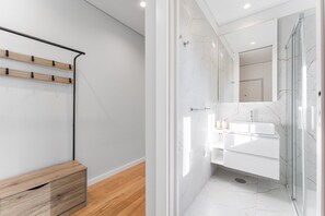 A modern bathroom with a glass shower enclosure, white marble tiles, and a minimalist sink area. - GuestReady - Porto Retreat with Terrace (Porto)