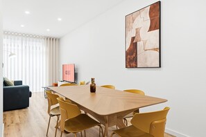 Et moderne værelse med et træspisebord, gule stole, en blå sofa og et fjernsyn, der viser "GUEST READY".