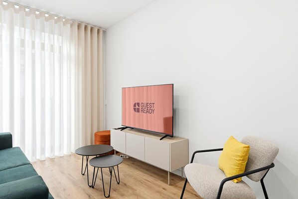 En moderne stue med et fladskærms-tv på et skab, en sofa, en stol med en gul pude og to små borde.