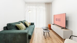 A modern living room with a green sofa, a small round table, and a flat-screen TV displaying "GUEST READY".