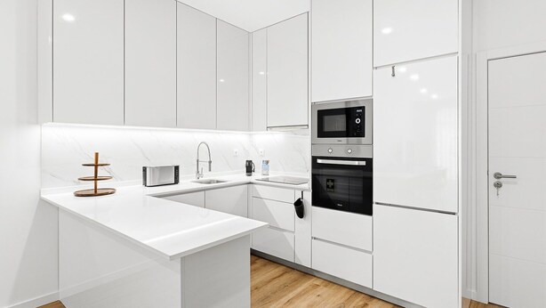 A modern kitchen with white cabinetry, a built-in oven, a microwave, and a coffee maker.