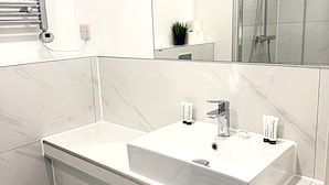 Un baño moderno con un lavamanos blanco, un espejo, una ducha y un inodoro.