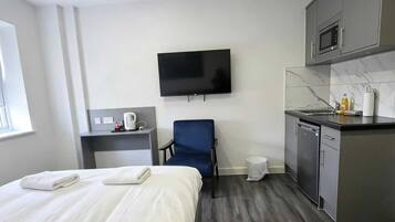 Habitación de hotel pequeña con cama, un escritorio, una silla, televisión y kitchenette.