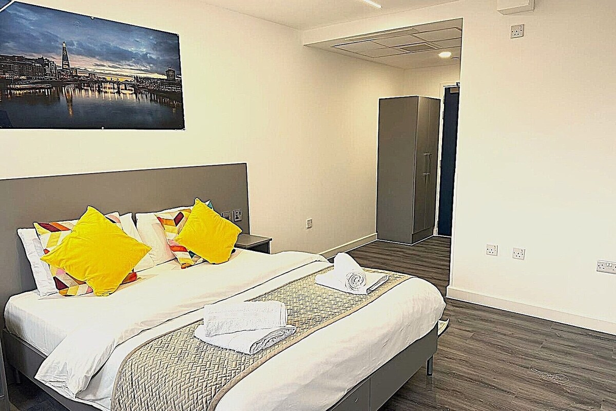 Ein Hotelzimmer mit einem Bett, einem Stadtbildgemälde, einem Kleiderschrank und einer Tür zu einem weiteren Raum.