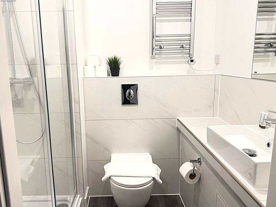 A bathroom with a glass shower enclosure, a toilet, a sink, and a small potted plant.