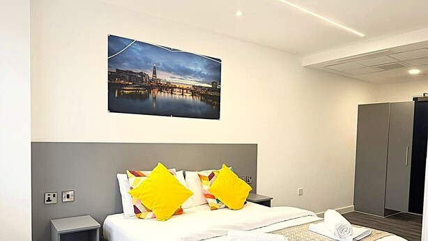 Habitación de hotel con cama, mesita de noche, armario y un cuadro de paisaje urbano en la pared.