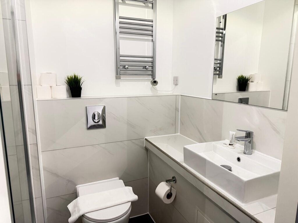 Een moderne badkamer met toilet, wastafel, spiegel, handdoekhouder en een kleine potplant.