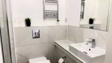 Un baño moderno con inodoro, lavamanos, espejo, toallero y una pequeña planta en maceta.