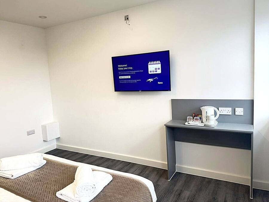 Una habitación de hotel con cama, escritorio, cafetera y televisor mostrando un mensaje de bienvenida.