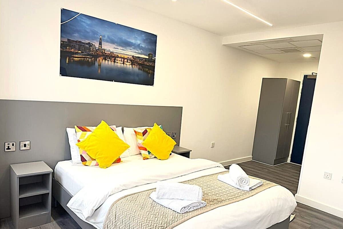 Quarto de hotel com cama, mesa de cabeceira, quadro pendurado na parede, guarda-roupa e porta.