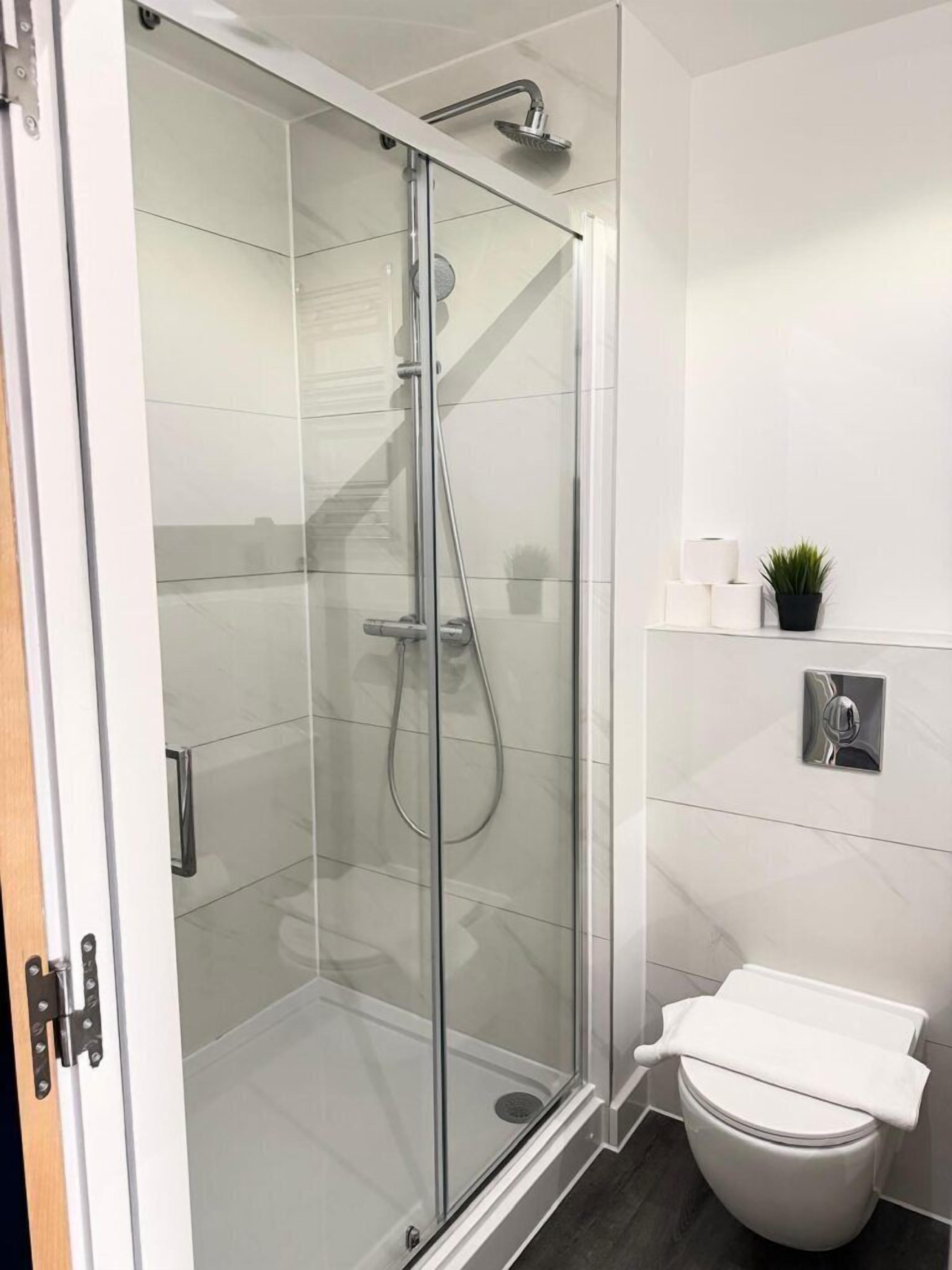 A modern bathroom with a glass-enclosed shower, a toilet, and a small shelf with toiletries.