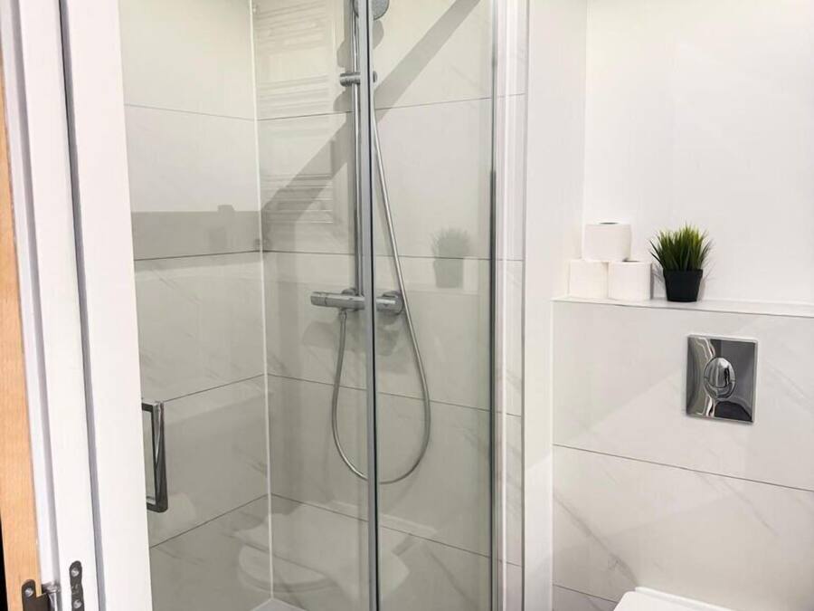 A modern bathroom with a glass-enclosed shower, a toilet, and a small shelf with toiletries.