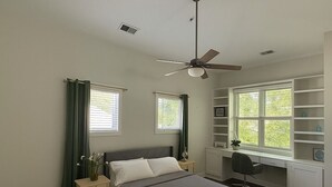 Un dormitorio con cama, escritorio y ventilador de techo.